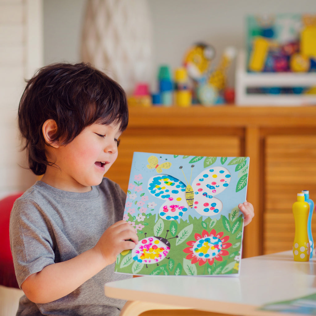 a boy looking at artwork where he applied dots of paint to an illustration of butterflies