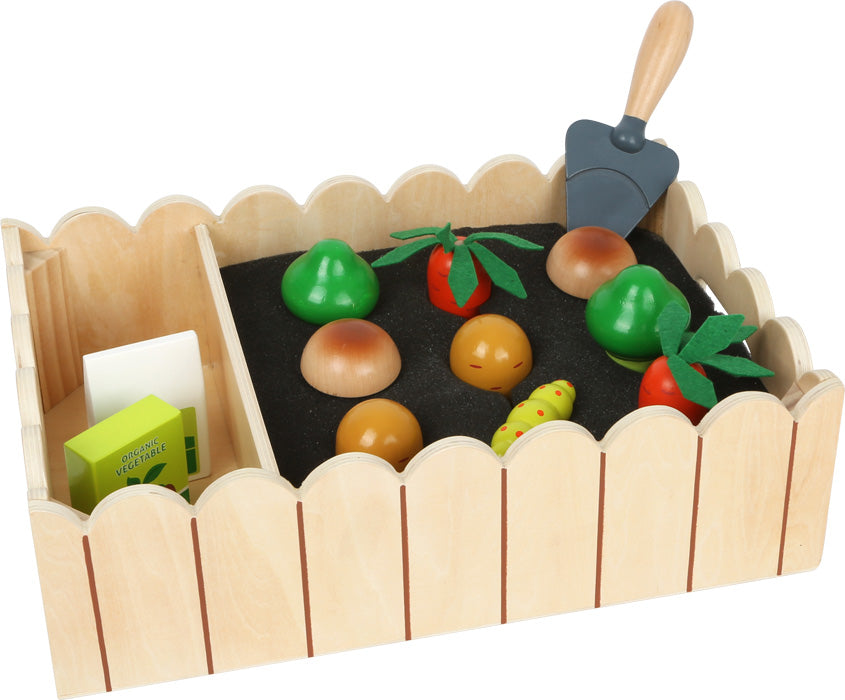 a toy wooden vegetable garden with fencing, and toy mushrooms, carrots, spade, and catepillar