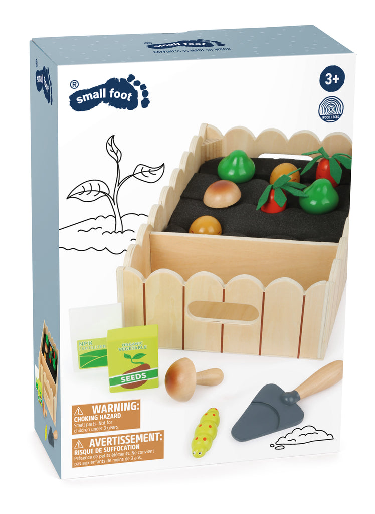 the package showing a toy wooden vegetable garden with fencing, and toy mushrooms, carrots, spade, and catepillar
