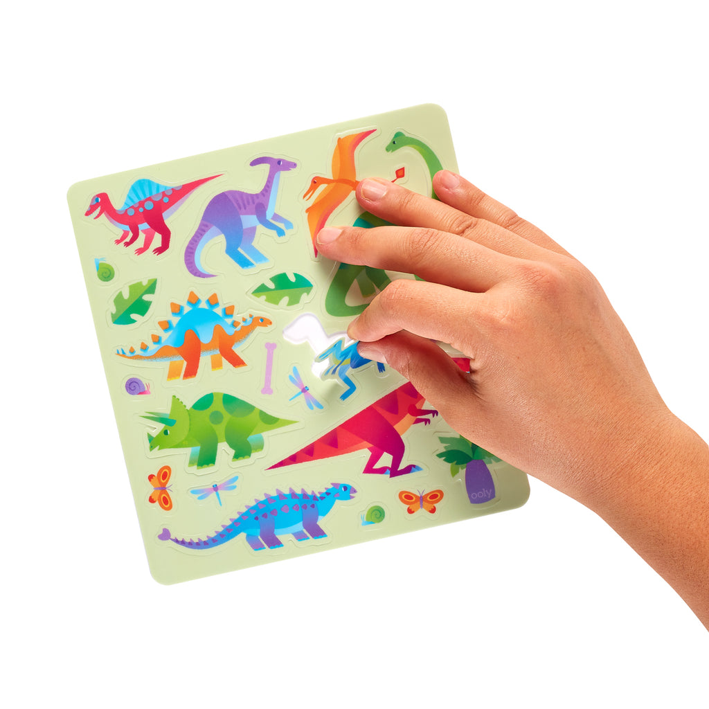 a hand peeling off a dinosaur sticker from a sticker sheet