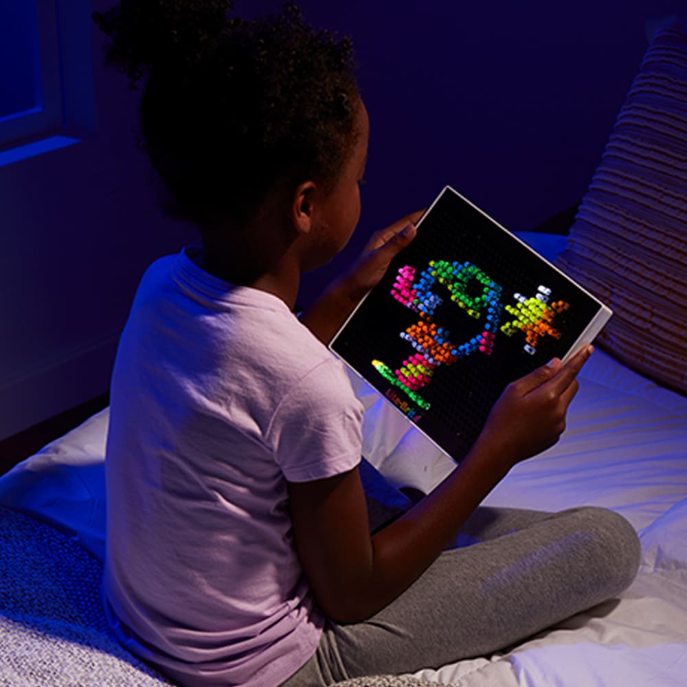a child looking at a lit up lite brite in a darkened room