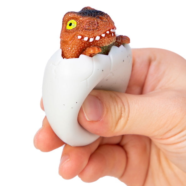 a hand squeezing a dinosaur egg with a little dinosaur head peeking out
