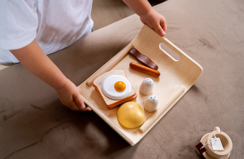 a boy holding the tray and wooden egg, sausage, toast, cheese, salt and pepper shakers