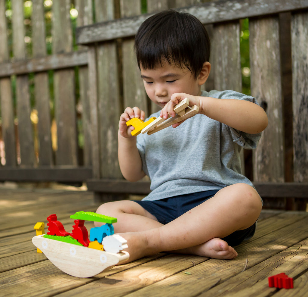 a child holding the tongs and a wooden giraffe with the balancing boat
