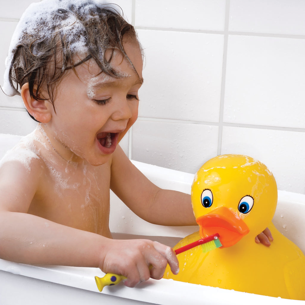 a toddler playing with the large rubber duck in a bathtub